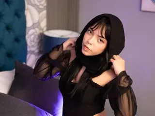 Young woman in a black hooded sheer top posing in a moody bedroom setting.