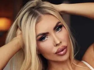 VioletchelseaBabesatation, a blonde woman, poses with her hands in her hair, looking directly at the camera with a pouty expression.