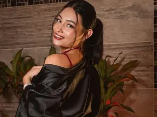 ViolettRouse smiles while looking over her shoulder, wearing a black satin top with her dark hair in a ponytail.