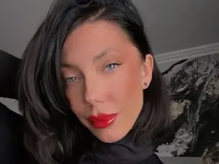 VivienneRuth poses with a direct gaze, showing her dark hair and red lipstick against a plain background.