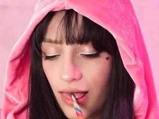 Vixen_Flutter wearing a pink velvet hood and looking down with a colorful lollipop in her mouth.