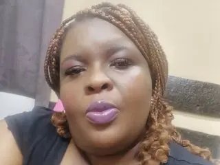 Close-up selfie of a woman with braided hair and pink lipstick posing indoors with a soft expression.
