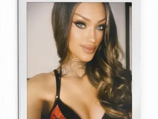 XBrielleMooreX poses with long wavy hair, wearing a black bra that shows off her cleavage and shoulders.