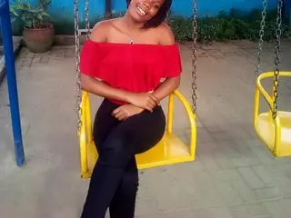 Xenatta poses sitting on a yellow swing wearing a red off-the-shoulder top and black pants, smiling at the camera.
