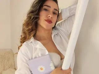 Young woman in a white button-down shirt holding a lavender clutch in a bright, minimalist indoor setting.