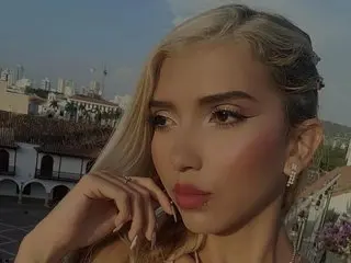 Ximena_Doll poses with a close-up headshot, showing her blonde hair and light makeup against a soft outdoor background.