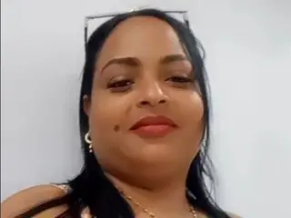 YANELISHOTT is a brunette woman with red lipstick and gold hoop earrings posing for a selfie against a white wall.
