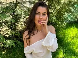 Beautiful woman in a white off-the-shoulder top posing thoughtfully in a lush green garden setting.