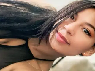 Young woman with long dark hair wearing a black halter top smiling in a bright, natural setting.