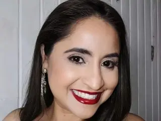 Smiling woman with dark hair and red lipstick wearing elegant silver earrings in a bright indoor setting.