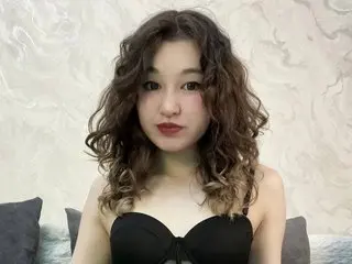 Young woman with curly brown hair wearing a black strapless top in a bright, minimalist room.
