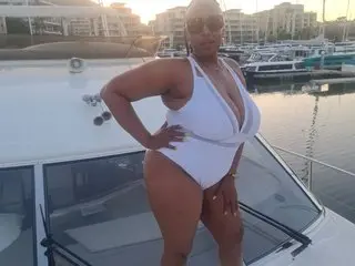 ZEEHD poses in a white one-piece swimsuit on a boat in a marina at sunset.