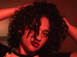 ZarahRosse poses with her dark curly hair framing her face, looking directly at the camera with a serious expression.
