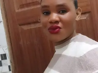 ZariaLuxe poses close-up, showing her face and shoulders, wearing a white and tan striped top with her dark hair pulled back.