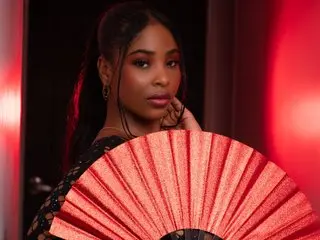 ZendayaRosse poses with a red fan, showing her face, dark hair, and shoulders against a red background.