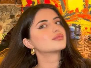 Zenvyra poses with long dark hair and gold hoop earrings, looking directly at the camera with a soft pouty expression.