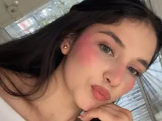 ZoeBarnett poses close-up with long dark hair and pink blush, looking into the camera with a soft expression.