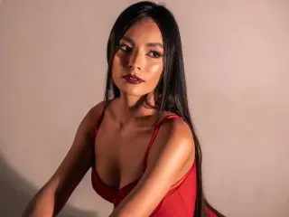 ZoeRuth poses with long dark hair, wearing a low-cut red bodysuit against a plain background.