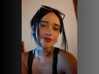 ZoeSalazar looks at the camera with a direct gaze, wearing a black tank top and sunglasses on her head, showing her neck tattoos and dark hair.