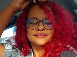 Zoe_Ross69 poses with her red hair and glasses, looking directly at the camera in a close-up shot.