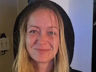 Smiling blonde woman in a black hooded sweatshirt relaxing indoors with a casual, cozy mood.
