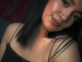 abbbiemoon poses close-up, showing her face, dark hair, and bare shoulders against a dark background.