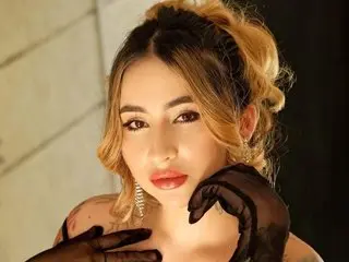 Glamorous woman with blonde wavy hair and black lace gloves posing in elegant evening attire.