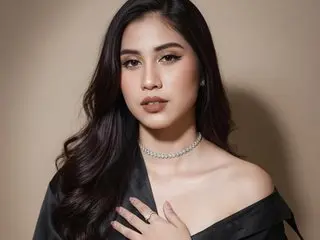 aithna_smitc poses with long dark hair and a black top, showing her shoulders and neck against a plain tan background.