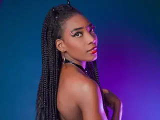 alexandracambell poses with her long dark braids, showing her bare shoulders and neck against a blue and purple lit background.