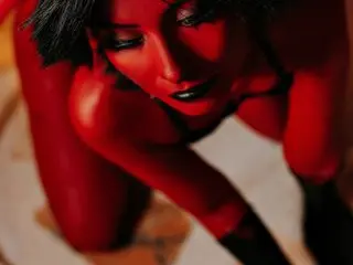alicejacob poses with red lighting, showing her face, hair, and bare shoulders in a dark setting.