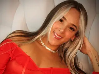 Smiling woman with blonde highlights in a red outfit posing against a white background.
