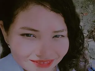 Smiling young woman with curly dark hair and red lipstick outdoors in natural sunlight.
