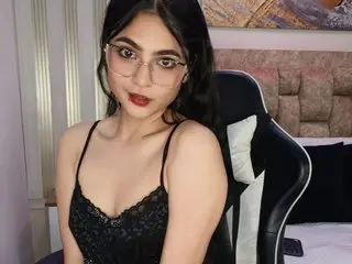 ariiel_bennet poses in a black lace camisole, looking at the camera with long dark hair and red lipstick.