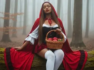 ashanty_1012 poses in a red hooded cloak and white blouse, holding a basket of red fruit against a misty forest background.