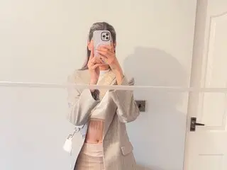 beautyheart28 poses in a tan blazer and matching skirt, holding a phone up to her face while standing in a bright room.