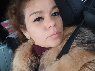 Woman in a luxurious brown faux fur coat sitting in a car with a thoughtful expression.