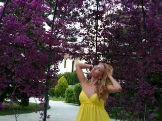 Blonde woman in a yellow summer dress posing under vibrant purple bougainvillea flowers in a sunny garden.