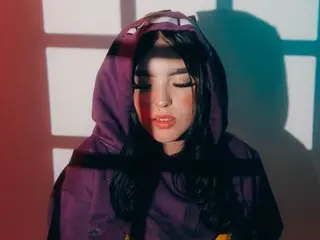 bubbleeAngel poses in a purple hooded jacket with her eyes closed against a shadowed wall.
