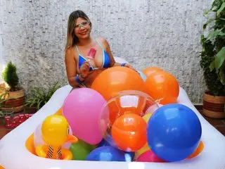bunny_blonde in a blue bikini sits behind a white inflatable pool filled with colorful pink, orange, and blue balloons.