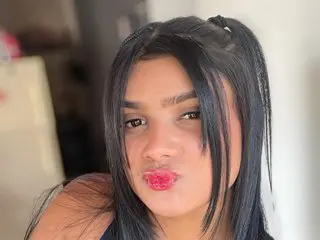 caroline_and_marcos has long dark hair and a light dusting of freckles on her nose while looking directly at the camera.