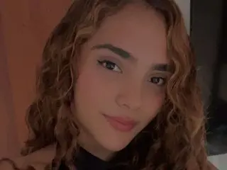 carolyne_18 looks at the camera with a slight smile, showing her wavy brown hair and makeup.