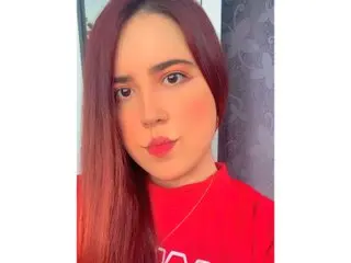 celeste67 poses with long red hair and red lipstick, looking directly at the camera in a close-up shot.
