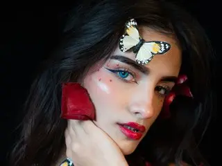charlott_22 poses with a butterfly clip in her dark hair, wearing red lipstick and pink blush.