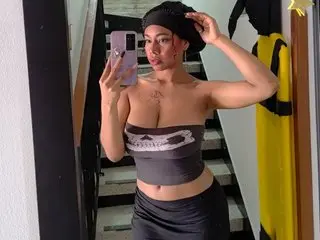 charlotte_bronte poses in a black tank top and black cap, showing her bare shoulders and chest in a mirror selfie.