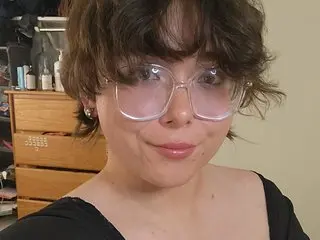 chubbymarysworld poses close-up with her dark wavy hair and glasses, looking directly at the camera with a slight smile.