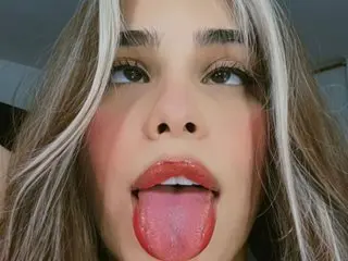 Close-up selfie of a young woman with blonde highlights and pink blush sticking her tongue out playfully.