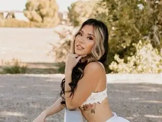 cuteskymk poses outdoors with long wavy hair, wearing a white lace bra that shows her cleavage and chest.