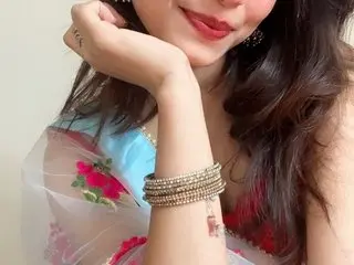 Smiling woman in traditional floral lehenga wearing gold bangles in a soft, elegant setting.