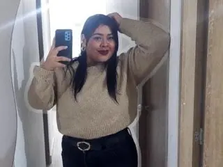 ema_foxyy poses for a mirror selfie wearing a tan sweater and black pants.