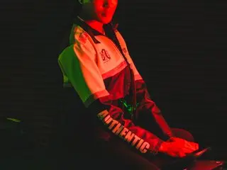 esmeraldabk poses in a bright green and white jacket with red accents, showing her hair and face under red lighting.